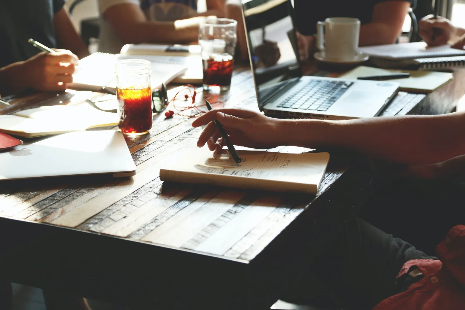 People working around a wooden table with laptops, notebooks and iced drinks